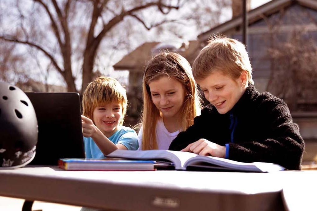 Three students sitting outside at a table studying on a laptop