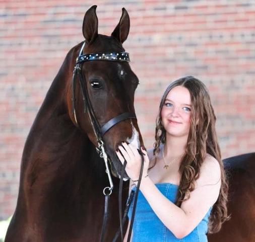 Fiona wearing a blue dress from TEC Connections Academy pictured here with her brown horse.